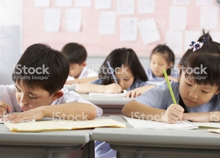 Group Of Students Working At Desks In A Chinese School Classroom Writing In Their Books